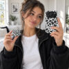 Woman holding a matching black-and-white leopard phone case and AirPods case Title: Matching Leopard Phone & AirPods Cases
