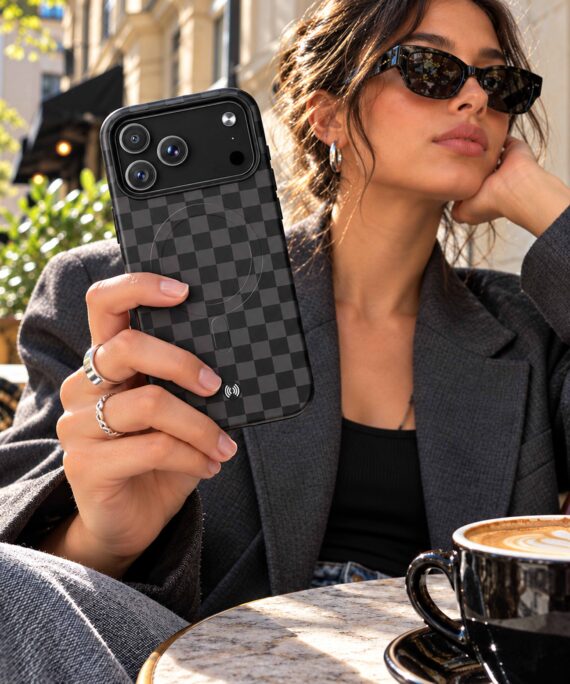 Person holding a charcoal checkerboard MagSafe phone case at an outdoor café